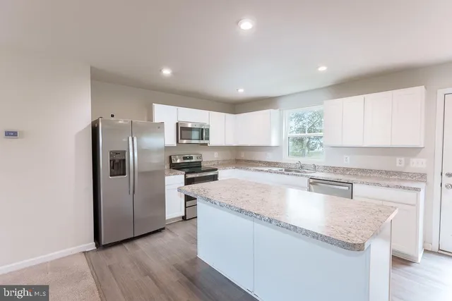 a kitchen with granite countertop stainless steel appliances a sink a refrigerator a center island and cabinets