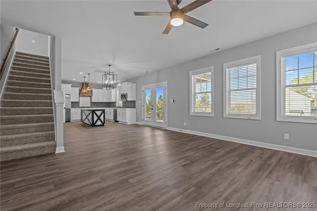 a view of a livingroom with wooden floor a ceiling fan and windows
