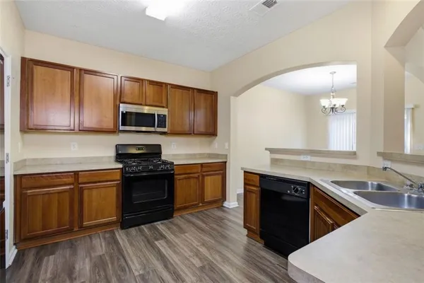 a kitchen with stainless steel appliances granite countertop wooden cabinets a stove top oven a sink and dishwasher with wooden floor