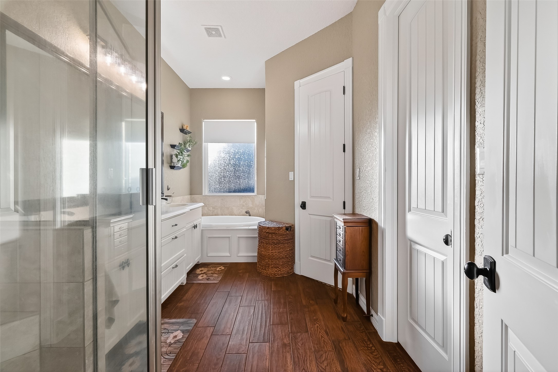 912 County Road 340 Angleton, TX 77515 - Photo 29 of 50 This bright bathroom features a spacious glass-enclosed shower, a white vanity with ample storage, a soaking tub, and elegant wood flooring. Natural light streams in through a frosted window, creating a serene and inviting atmosphere.