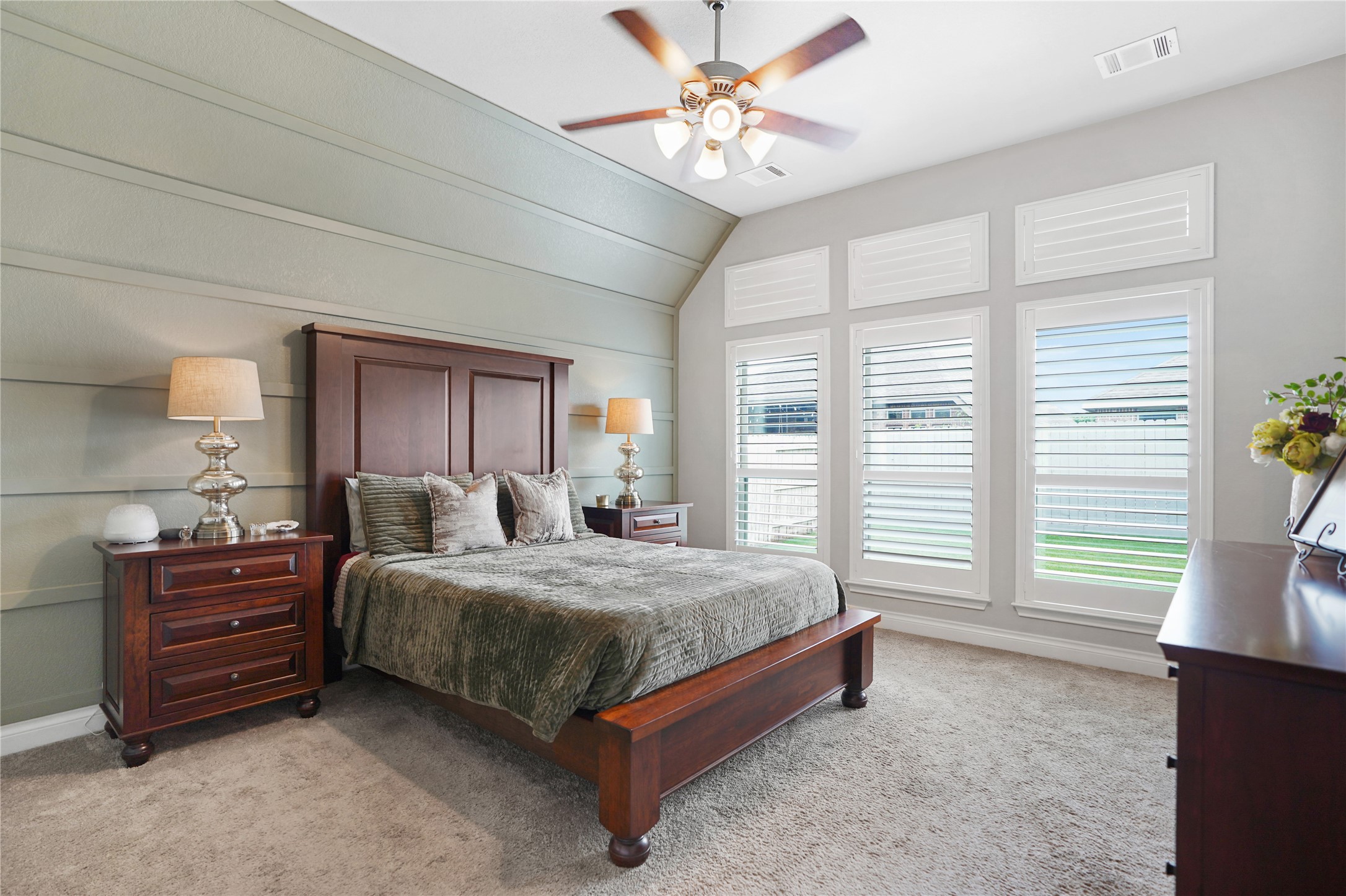 2345 Redwood Ridge Trail Manvel, TX 77578 - Photo 24 of 39 This inviting bedroom features a cozy carpet, a stylish wood bed frame, and matching nightstands with lamps. The room is brightened by large windows with shutters and is complemented by a ceiling fan, creating a comfortable and elegant space.
