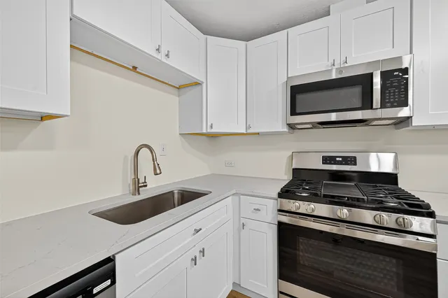 a kitchen with stainless steel appliances granite countertop white cabinets a stove a sink and dishwasher