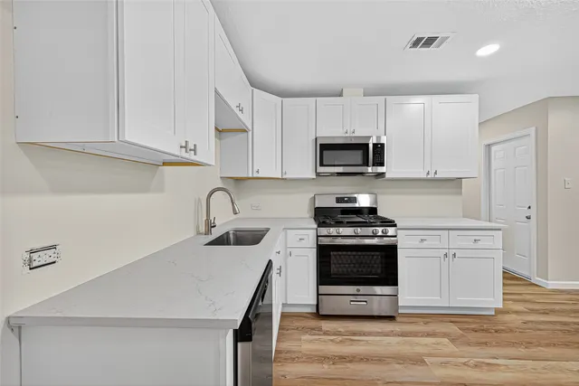 a kitchen with stainless steel appliances granite countertop a stove a sink dishwasher and a refrigerator with white cabinets