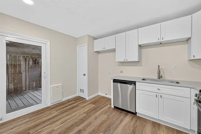 a kitchen with stainless steel appliances granite countertop a dishwasher a stove a sink and white cabinets with wooden floor