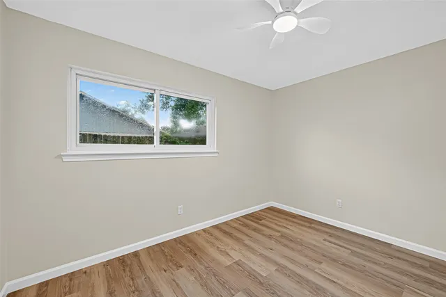 a view of an empty room with wooden floor and a chandelier fan