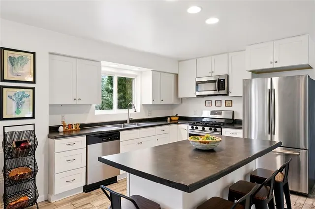 a kitchen with stainless steel appliances a stove a sink a refrigerator white cabinets a dining table and chairs