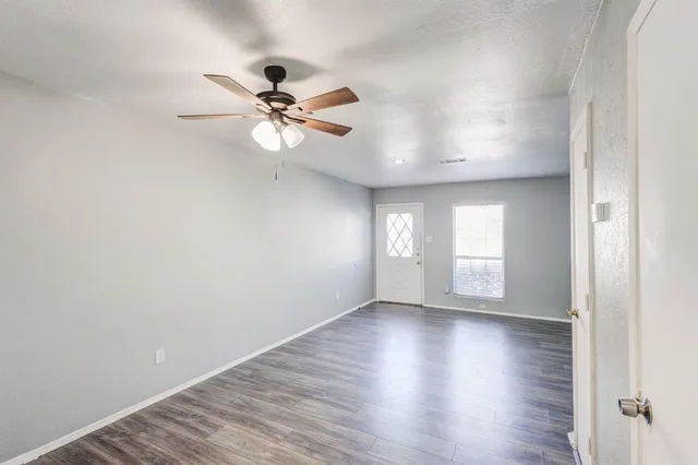 an empty room with wooden floor fan and windows