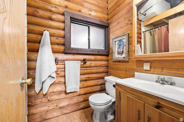 4725 Pine Ridge Road Evanston, UT 82930 - Photo 28 of 82 Bathroom featuring natural wood plank and log walls, a white toilet, and a vanity with a white countertop and natural wood cabinetry