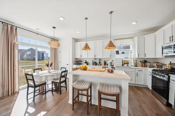 a kitchen with stainless steel appliances granite countertop a stove a sink a refrigerator a dining table and chairs with wooden floor