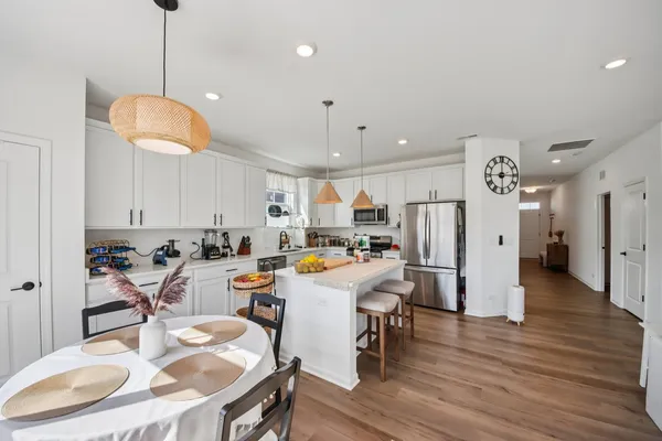 a room with stainless steel appliances kitchen island granite countertop a dining table chairs and a refrigerator