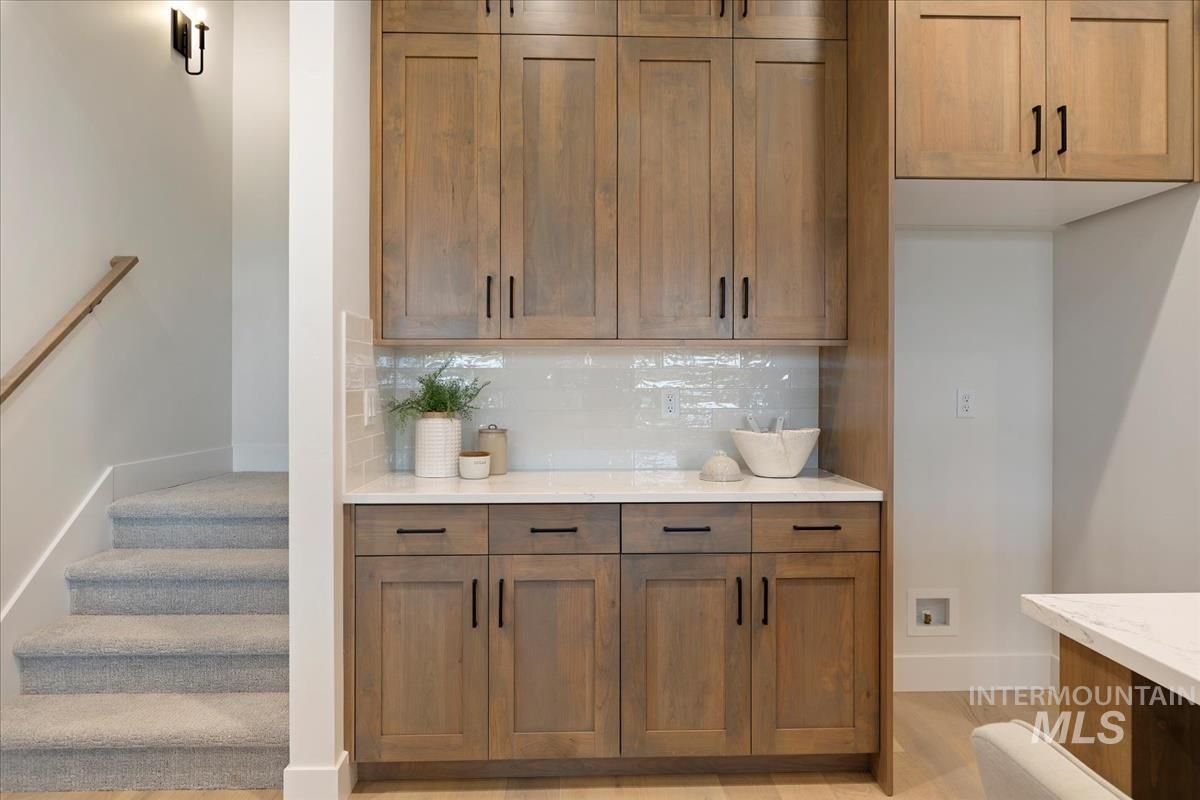 232 South Fusion Avenue Kuna, ID 83634 - Photo 16 of 30 Bar area featuring decorative backsplash, brown cabinets, light stone countertops, and stairs