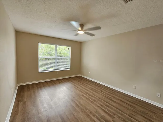 an empty room with wooden floor ceiling fan and windows