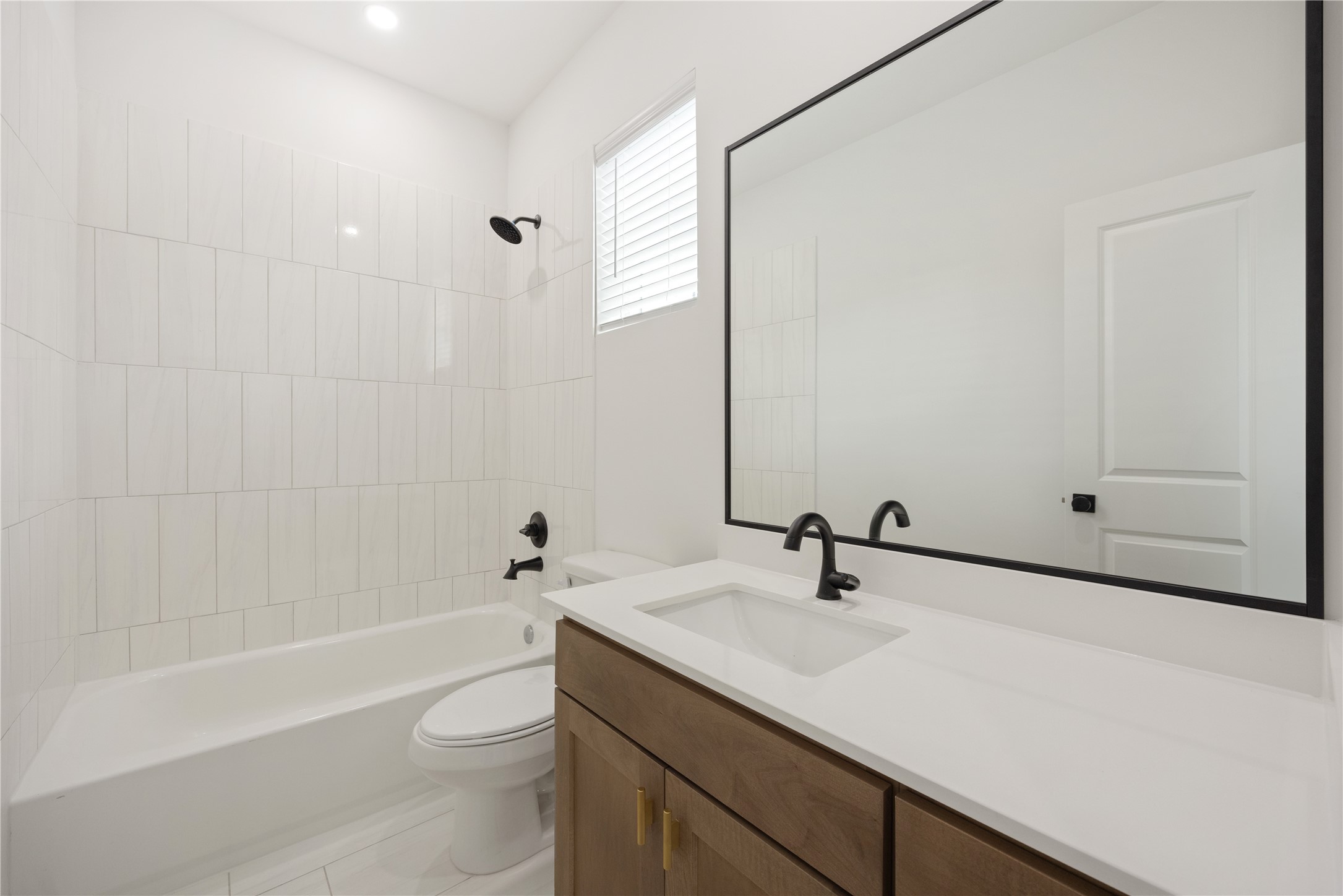 2121 Hoskins Drive, Unit C Houston, TX 77080 - Photo 10 of 34 The first-floor full bath showcases a fresh, modern design with a wood vanity, white countertop, black fixtures, large framed mirror, and tub/shower combination with vertical tile surround. A window brings in natural light, creating a bright and functional bath for guests or the adjacent bedroom.