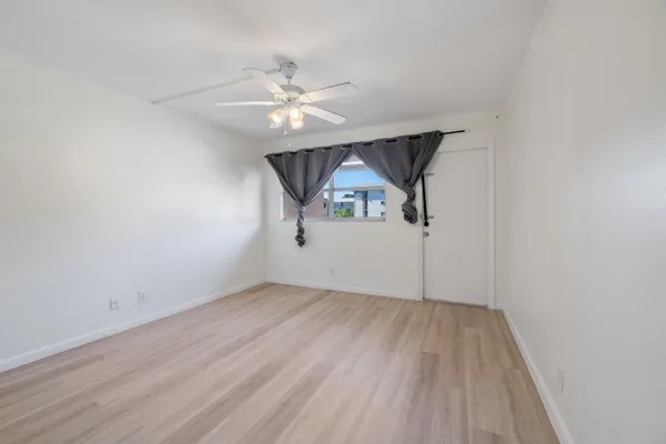 an empty room with wooden floor chandelier fan and windows