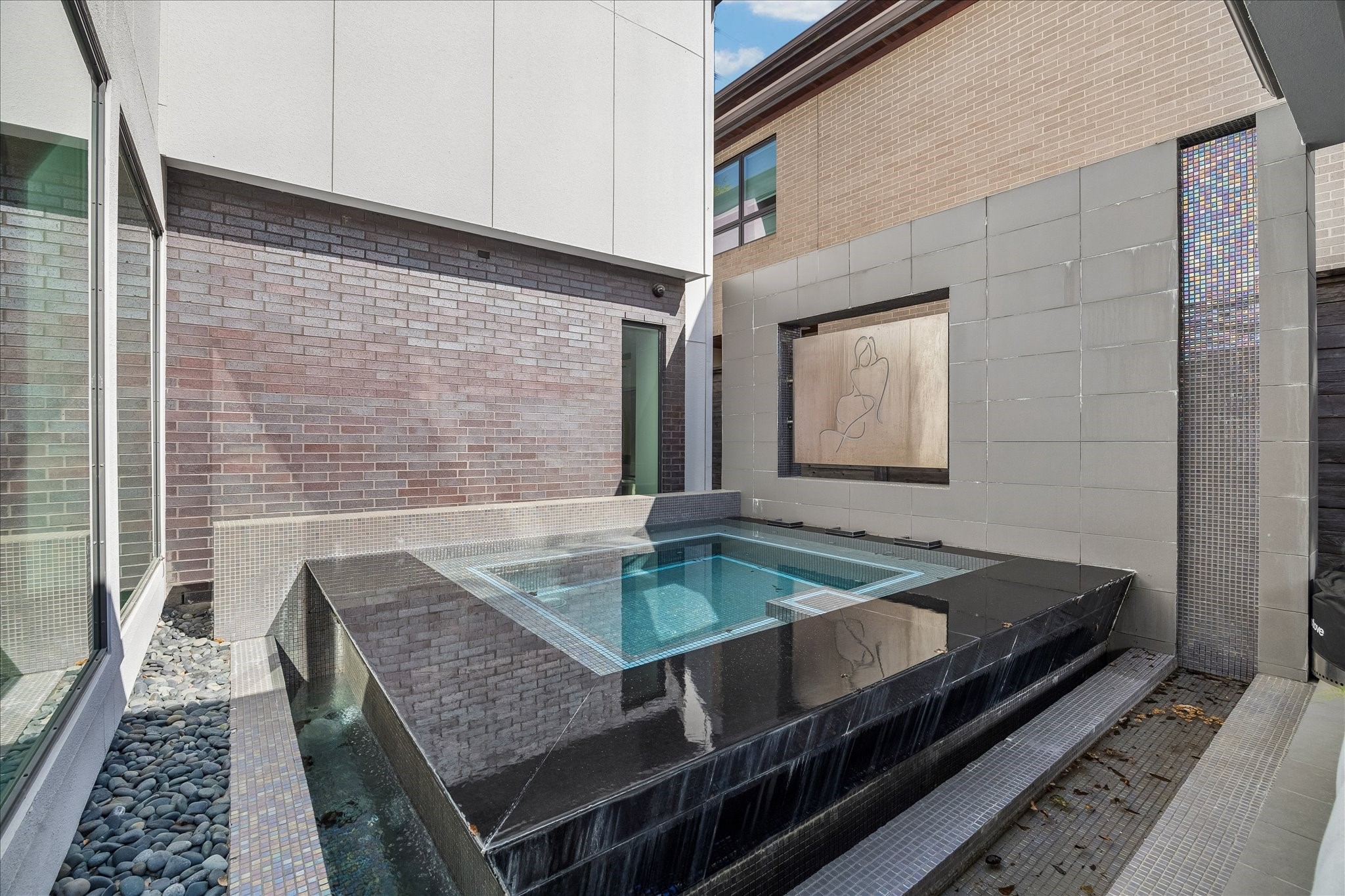 2014 Park Street Houston, TX 77019 - Photo 14 of 40 This modern home features a sleek outdoor Pool with a waterfall edge, surrounded by contemporary brick and tile accents, creating a serene and stylish retreat.