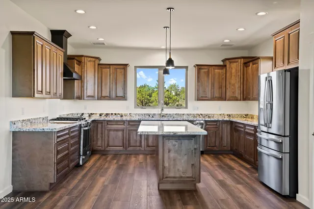 a kitchen with stainless steel appliances granite countertop a refrigerator a sink dishwasher a stove and white countertops with wooden floor