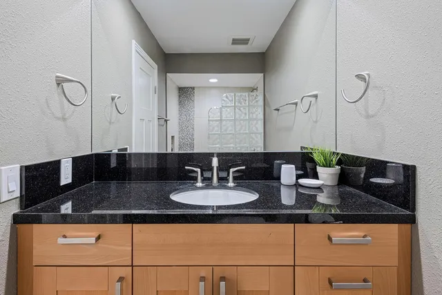 a bathroom with a granite countertop sink a mirror and shower