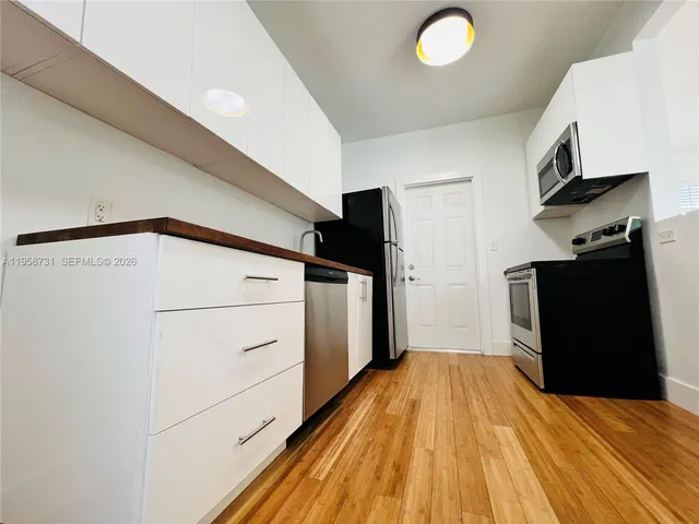 a view of a refrigerator in kitchen and an empty room with wooden floor