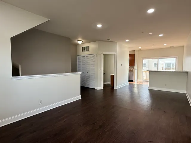 a view of an empty room with wooden floor and a kitchen