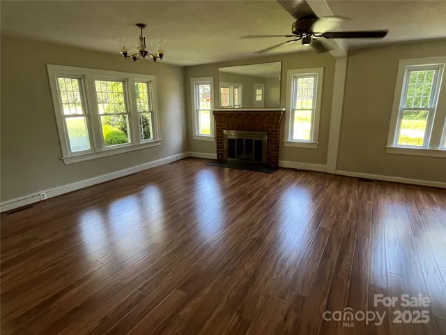 a view of an empty room with wooden floor fireplace and a window