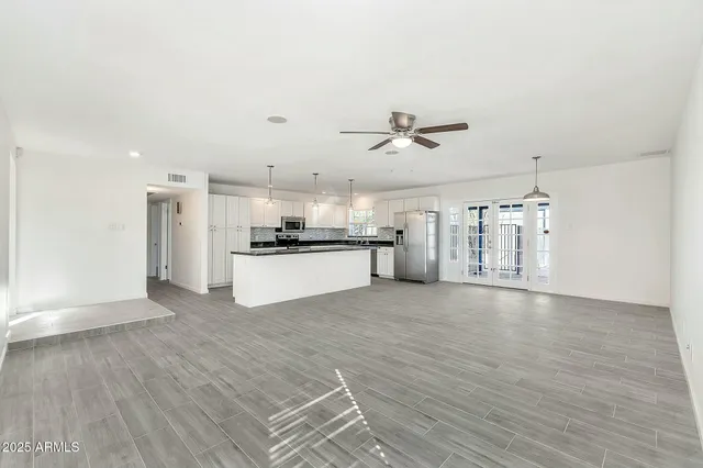 a large kitchen with stainless steel appliances a large counter top a stove a refrigerator white cabinets and wooden floor