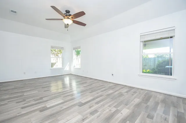 an empty room with wooden floor chandelier fan and windows