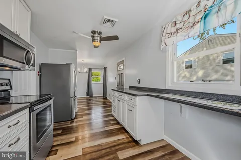 a kitchen with granite countertop a refrigerator a stove and white cabinets with wooden floor