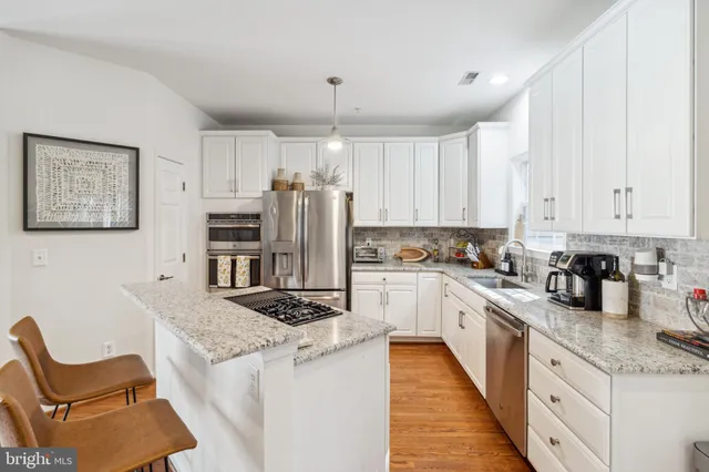 a kitchen with granite countertop a refrigerator a stove a sink dishwasher and white cabinets with wooden floor