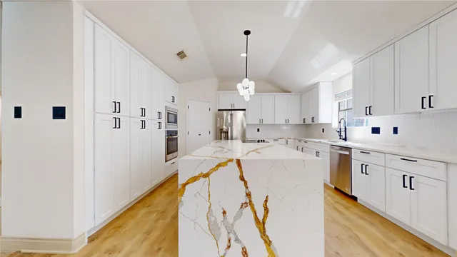a large white kitchen with a large island oven a stove and a sink with cabinets