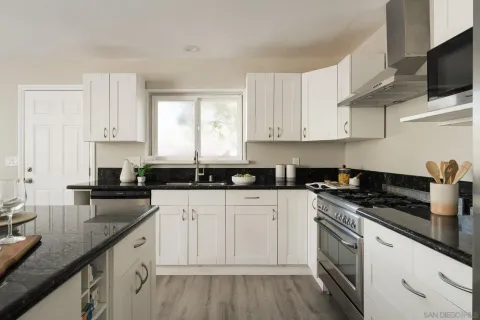 a kitchen with granite countertop a sink dishwasher stove and white cabinets with wooden floor