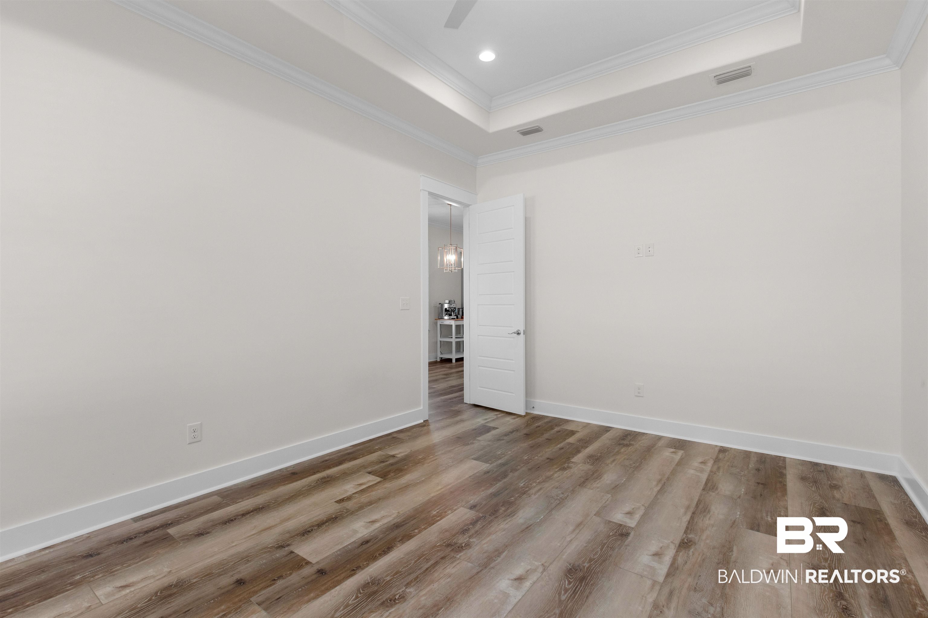 8069 Carmel Circle Foley, AL 36535 - Photo 16 of 23 Spare room featuring baseboards, crown molding, wood finished floors, and a raised ceiling
