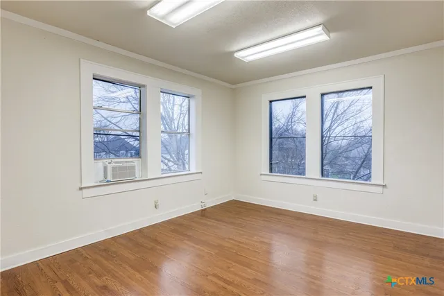 a view of an empty room with wooden floor and a window