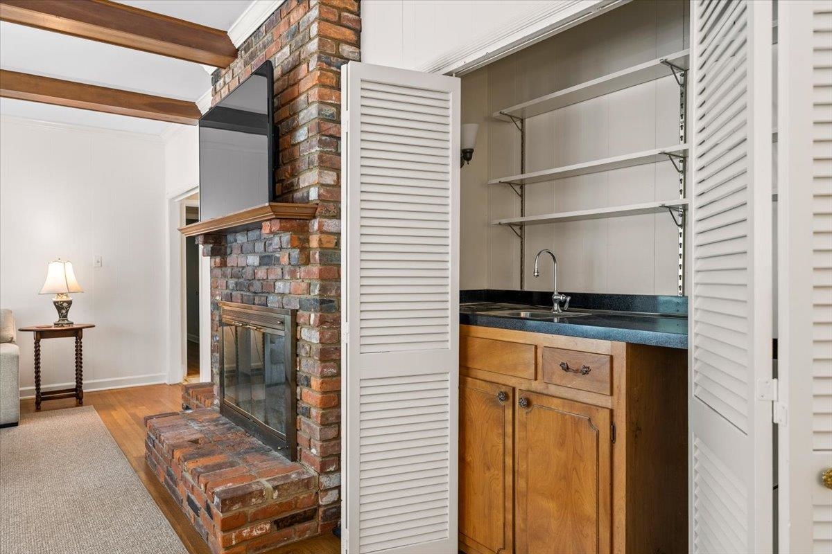1273 Brookfield Road Memphis, TN 38119 - Photo 14 of 40 Brick fireplace with a wooden mantel and a built-in wet bar featuring a dark countertop, stainless steel sink, and wood cabinetry, all concealed by louvered bi-fold doors