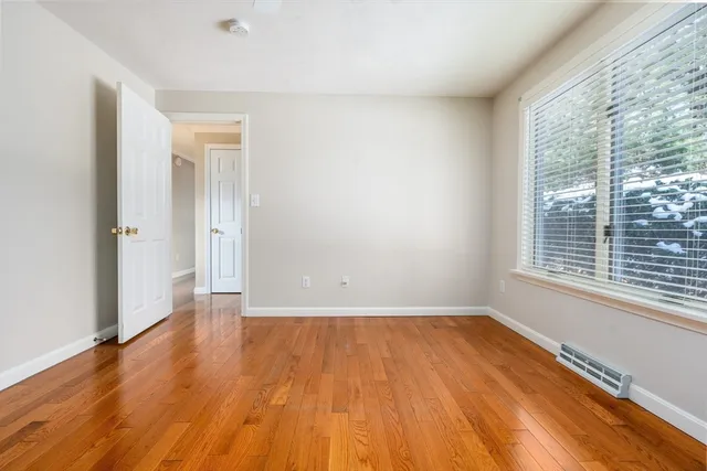 a view of an empty room with wooden floor and a window