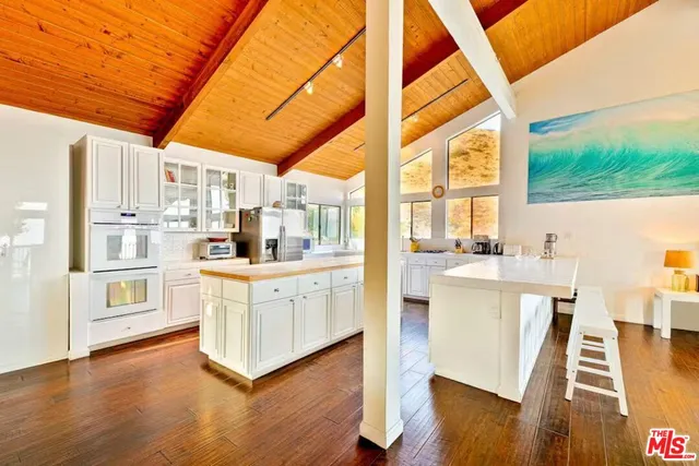 a large white kitchen with stainless steel appliances wooden floors and white walls