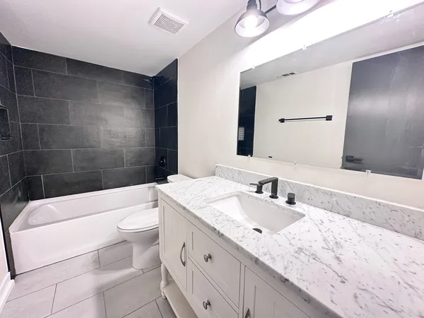 a bathroom with a granite countertop bathtub sink vanity mirror and toilet