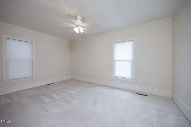 an empty room with a chandelier fan and windows