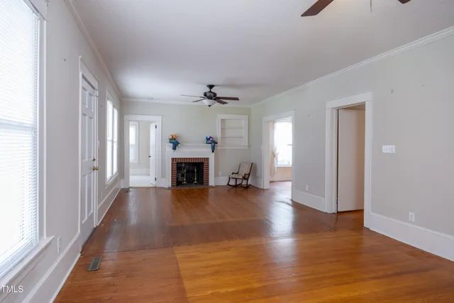 a view of an empty room with wooden floor fireplace and a window