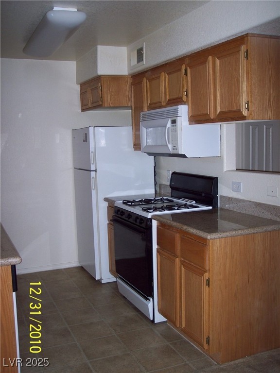 3318 North Decatur Boulevard, Unit 2077 Las Vegas, NV 89130 - Photo 12 of 19 Kitchen featuring gas range, white microwave, brown cabinets, and dark tile patterned flooring