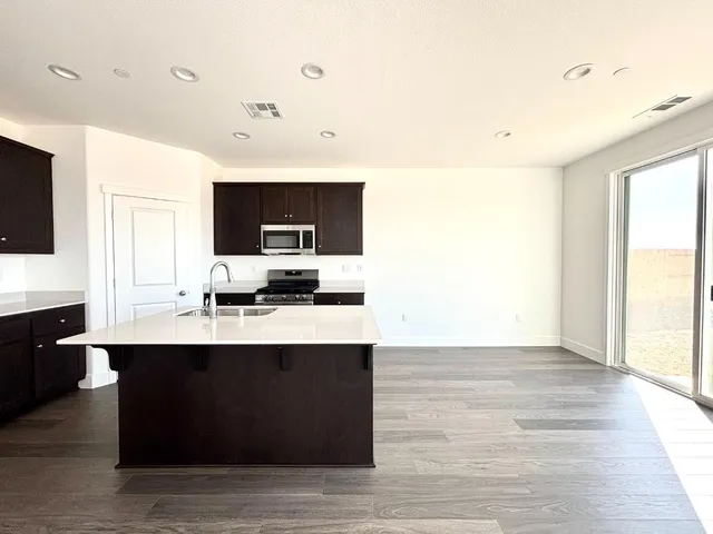 a open kitchen with stainless steel appliances granite countertop a sink dishwasher a microwave oven and a refrigerator with wooden floor