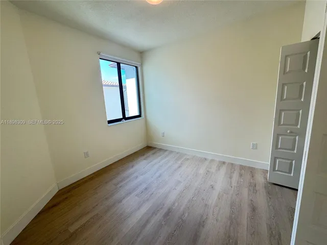 a view of an empty room with a window and wooden floor