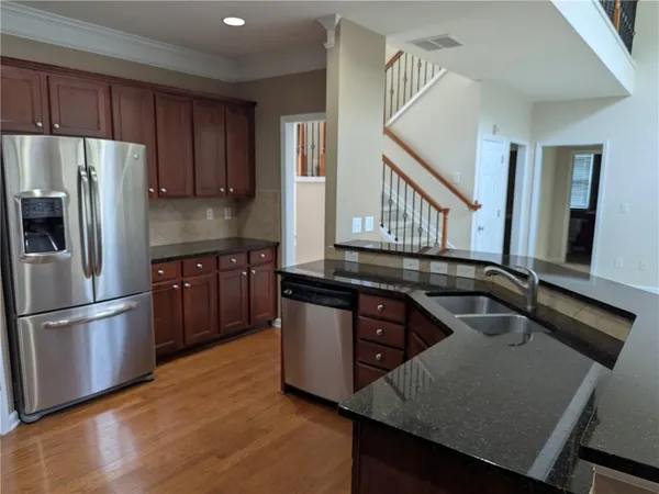 a kitchen with stainless steel appliances granite countertop a refrigerator a sink dishwasher a stove and white countertops with wooden floor