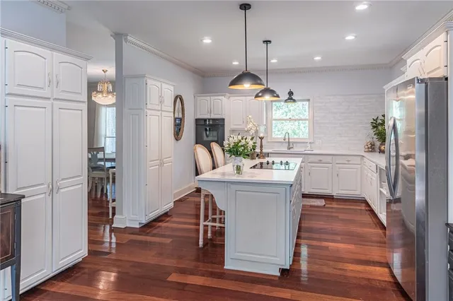 a kitchen with stainless steel appliances kitchen island granite countertop a refrigerator a oven a sink dishwasher and white cabinets with wooden floor