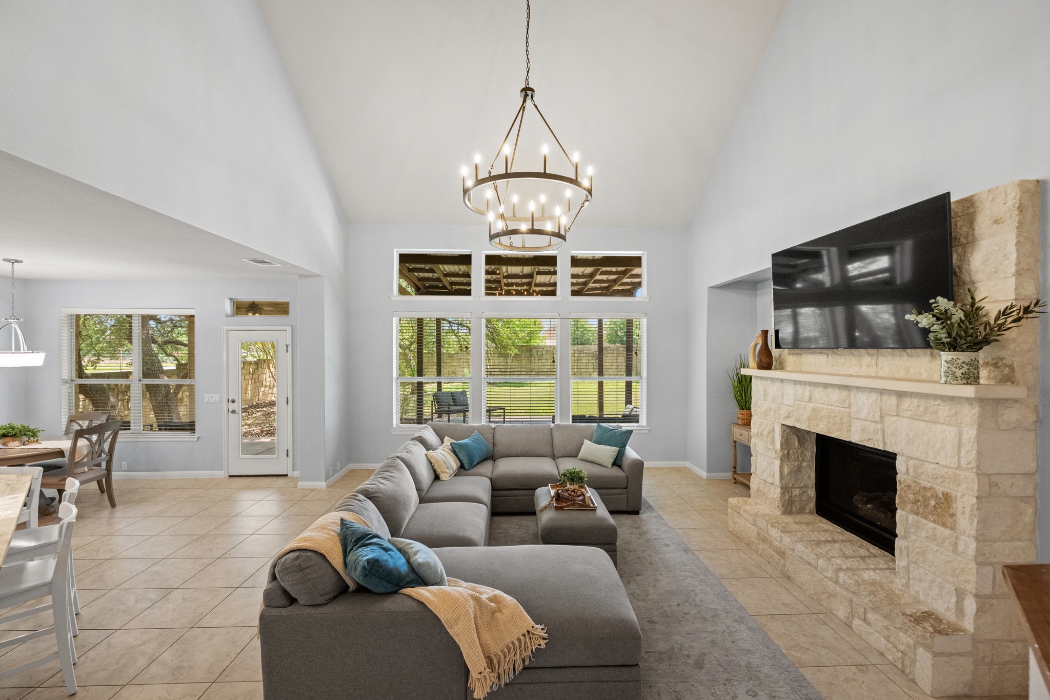 1023 Grassy Field Road Austin, TX 78737 - Photo 8 of 40 Vaulted ceiling living area featuring a stone-clad fireplace, tile flooring, and multiple windows overlooking outdoor areas