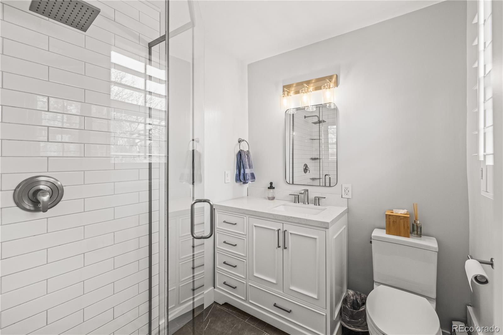7005 West 44th Avenue Wheat Ridge, CO 80033 - Photo 15 of 37 a bathroom with a toilet a sink a mirror and shower