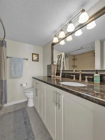 a bathroom with a granite countertop sink a toilet a mirror a vanity and shower