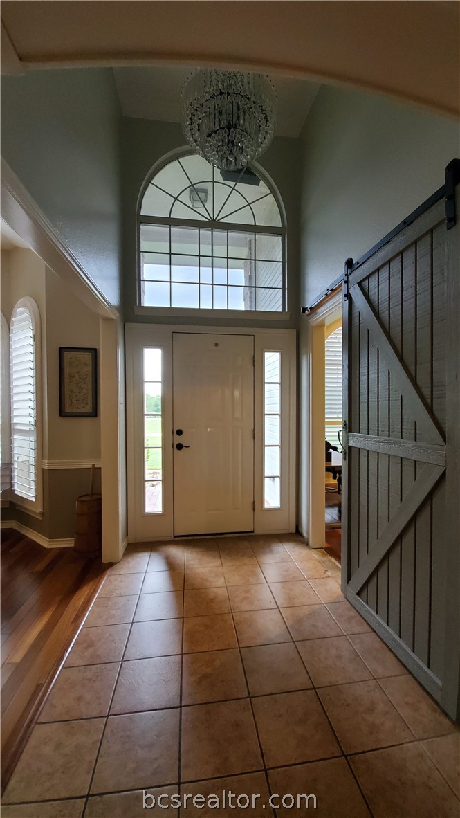 5660 Falling Water Bryan, TX 77808 - Photo 5 of 27 Foyer entrance with a high ceiling, an inviting chandelier, a barn door, and hardwood / wood-style floors