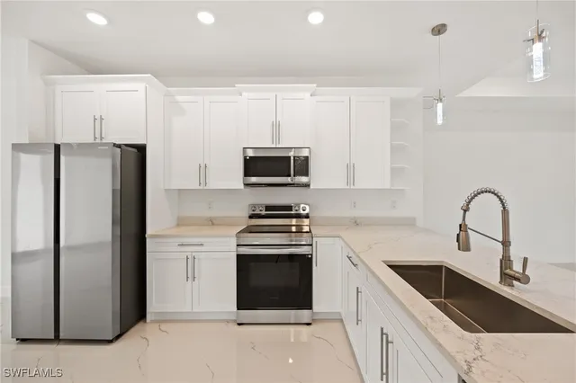 a kitchen with stainless steel appliances granite countertop a refrigerator stove a sink and white cabinets