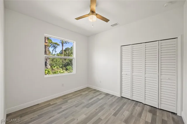 an empty room with wooden floor chandelier fan and windows