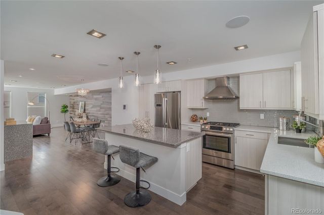 a kitchen with stainless steel appliances granite countertop a stove top oven a sink a dining table and chairs with wooden floor